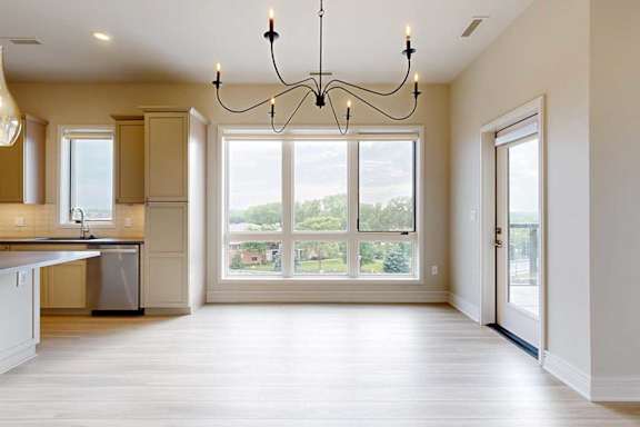 A dining room with a chandelier, a 3-pannel floor-to-ceiling window, and a windowed door to the balcony.