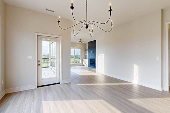 A large dining room with a wire chandelier and hardwood-style flooring, open to a spacious living room.