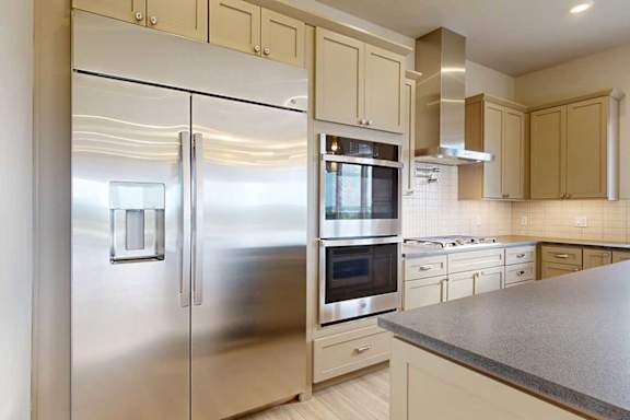 A gourmet kitchen with an oversized stainless steel fridge, two stainless steel ovens, and taupe cabinets.