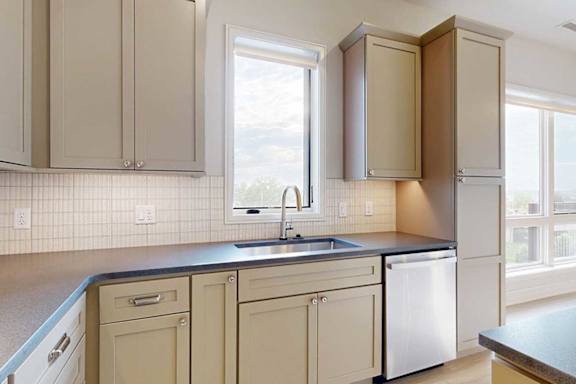 A gourmet kitchen with taupe cabinetry, quartz countertops, a tile backsplash, and a window over the kitchen sink.