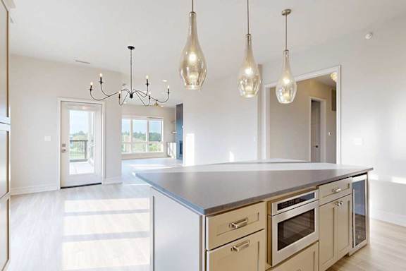 A modern kitchen island with a built-in microwave and wine fridge, with pendant lighting, open to a dining room and living room.