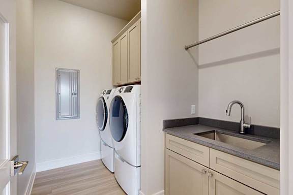 A laundry room with a full-sized front-loading washer and dryer with overhead cabinetry for storage, and a utility sink with quartz counters.