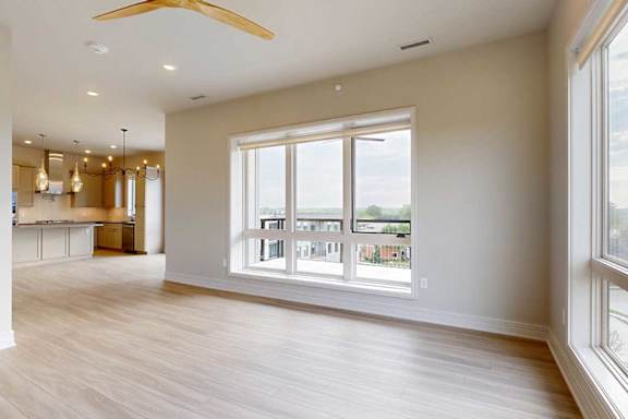 A modern living room with hardwood-style flooring, two floor-to-ceiling windows, and a large ceiling fan.