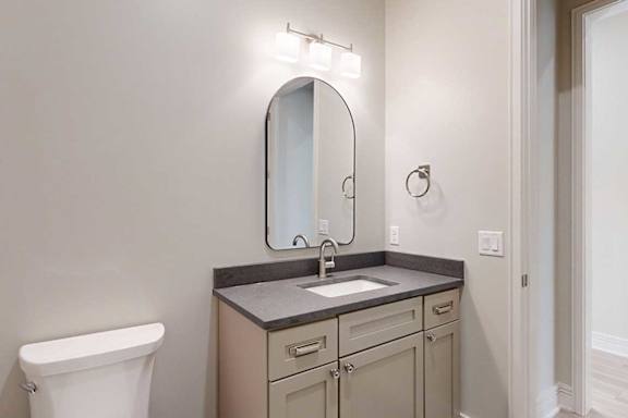 A half bathroom with a quartz vanity sink and a mirror with overhead lighting.