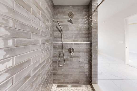 A tiled walk-in shower with a half wall, glass window, and a shower head with detached sprayer.
