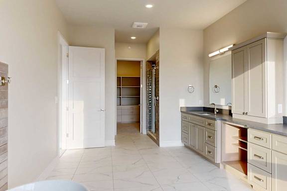 A spacious ensuite bathroom with a double vanity sink, walk-in shower, soaking tub, and attached dressing room.