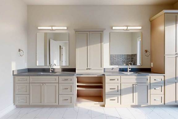 A spacious ensuite bathroom featuring a quartz double vanity with taupe cabinetry, a tall storage cabinet, and tiled flooring.