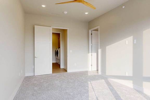 A carpeted bedroom with ensuite bathroom, attached dressing room, and a ceiling fan.