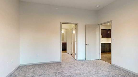 a bedroom with white walls and carpeted floor with two open doors