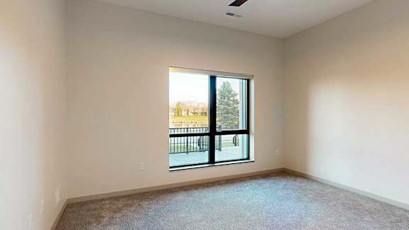 a bedroom with carpeted flooring and a large window looking out to the walk-out patio