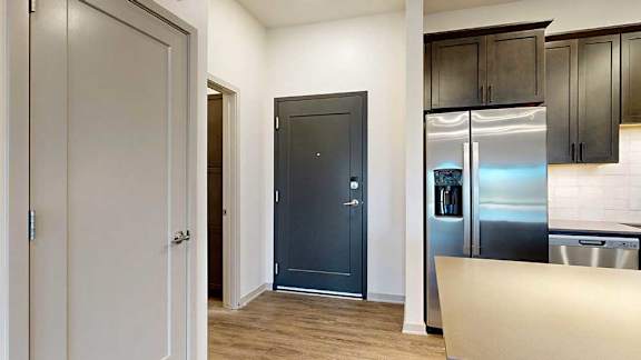 a front door next to a kitchen with a stainless steel fridge and a mechanical closet