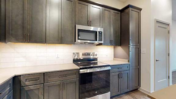 a kitchen with dark cabinets, white quartz countertops, and stainless steel microwave and oven