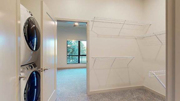 a walk-through closet with a washer and dryer and a doorway leading to the bedroom