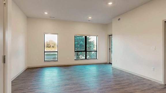 a large living room with hardwood floors, two windows, and a door leading out to the patio