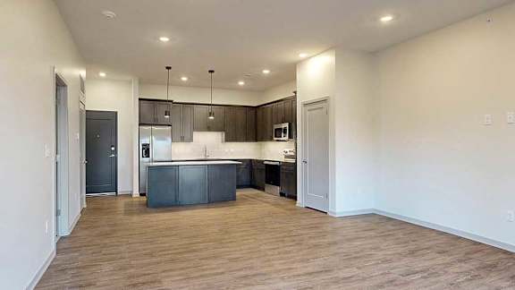 an open living room next to a kitchen with dark cabinets and a large central island