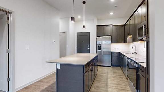 a modern kitchen with a large island and stainless steel appliances in front of an entry way