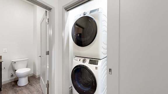 a white stackable washing machine and dryer in a laundry room next to a bathroom