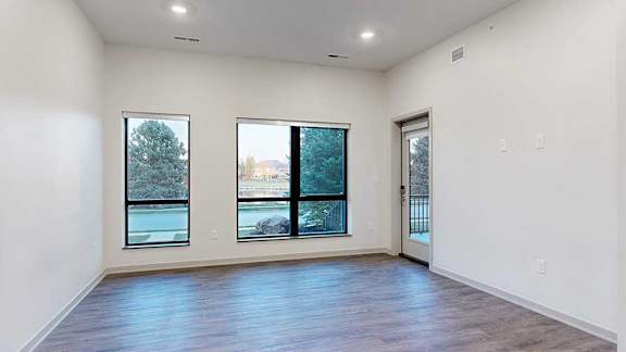 a spacious living room with a door and two large windows