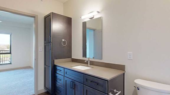 a bathroom with a wide quartz vanity sink, mirror, and tall storage cabinet