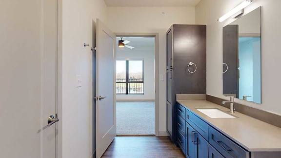 a bathroom with a wide quartz vanity sink, mirror, and a door leading to a bedroom