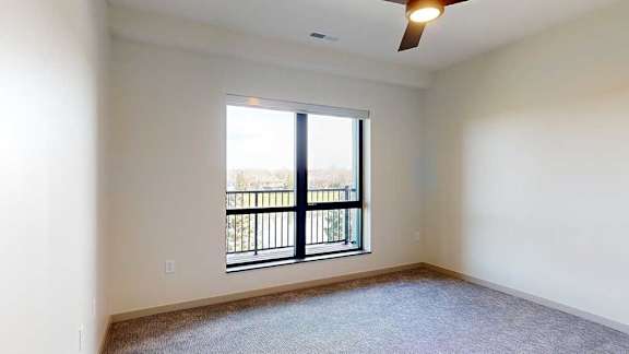 a bedroom with a ceiling fan and a window overlooking a balcony