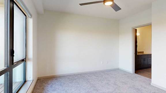 a bedroom with a ceiling fan, an attached bathroom, and a large window