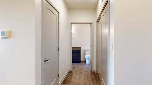 a hallway with a closed coat closet, a closed laundry closet, and an open door to a bathroom