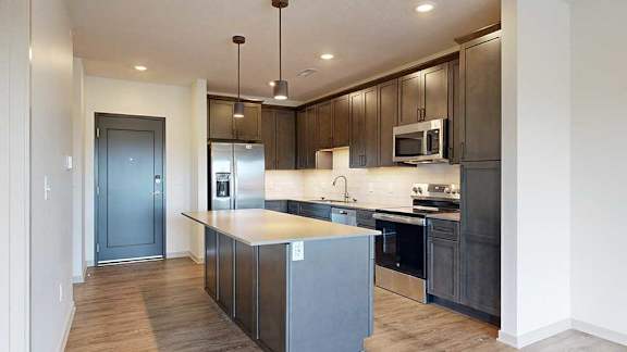 a modern kitchen with dark wood cabinets, light quartz countertops, a large central island, a tile backsplash, and stainless steel appliances