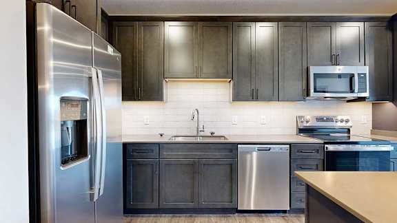 a modern kitchen with dark wood cabinets, a light tile backsplash, quartz countertops, and stainless steel appliances