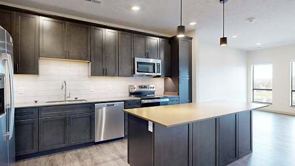a modern kitchen with dark wood cabinets, light quartz countertops, a large central island, a tile backsplash, and stainless steel appliances