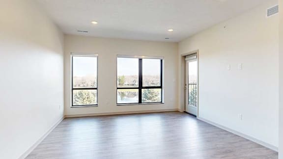a living room with hardwood flooring, two large windows, and a door to the balcony