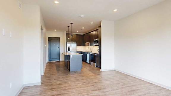 a living room with hardwood flooring next to a modern kitchen with dark wood cabinets and stainless steel appliances