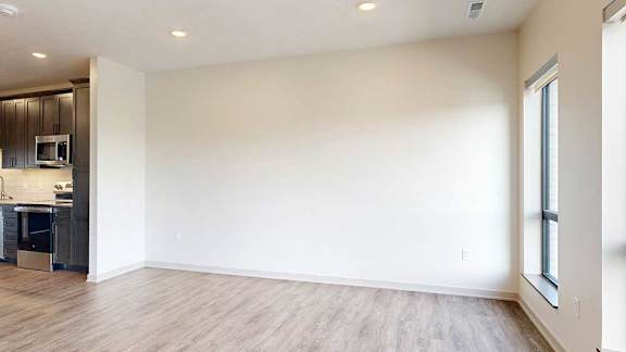a living room with hardwood flooring, two windows for natural light, and a wide white wall