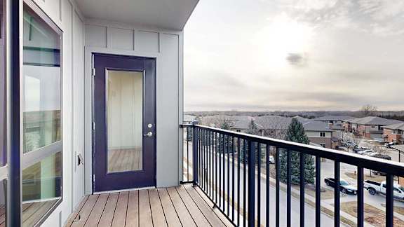 A balcony with a black metal railing, a windowed door to the living room, and a window into the bedroom.