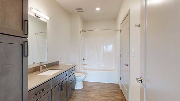 A bathroom with a wide quartz vanity, dark cabinets, and a tub shower with chrome fixtures.