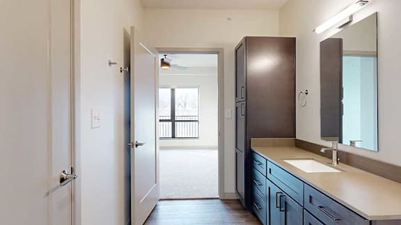 A walk-through bathroom with a wide quartz vanity and a door open to a bedroom.