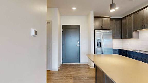 A front entryway next to a modern kitchen with dark cabinets and stainless steel appliances.