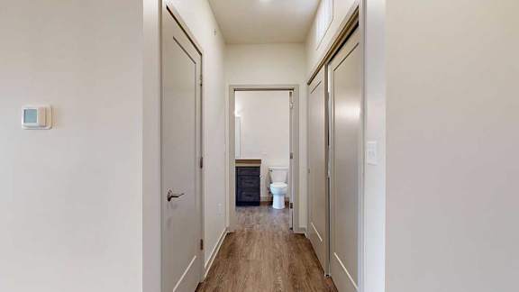 A hallway with closets on either side, and an open door to a bathroom at the end.