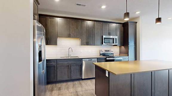 A kitchen with dark wooden cabinets, quartz countertops, a central island, and stainless steel appliances.