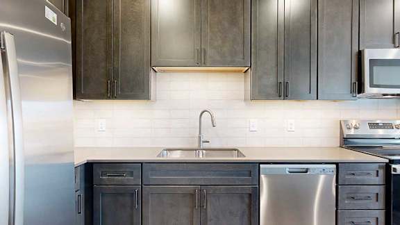 A modern kitchen sink with quartz counters, dark wooden cabinets, and a tile backsplash.