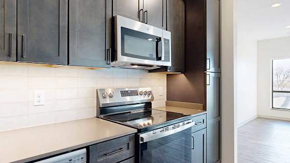 A close up of the stainless steel microwave and range in a kitchen with dark wooden cabinets.