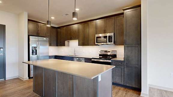 A kitchen with dark wooden cabinets, quartz countertops, a central island, and stainless steel appliances.