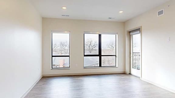 A living room with hardwood-style flooring and floor-to-ceiling windows.