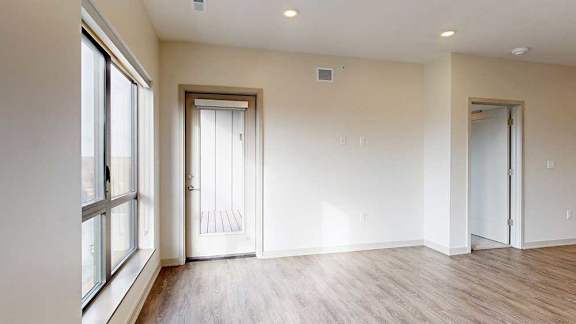 A living room with hardwood-style flooring, floor-to-ceiling windows, and a windowed door to the balcony.