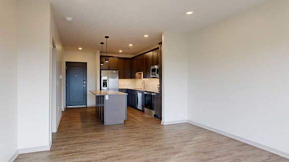 A living room with hardwood-style flooring and kitchen with dark wooden cabinets.