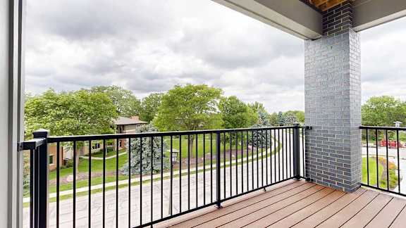 A balcony with a black metal railing, a brick pillar and a view of the neighborhood.