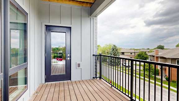 A balcony with a black metal railing, a windowed door to the living room, and a view of the neighborhood.