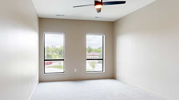 A carpeted bedroom with a ceiling fan and two tall windows.