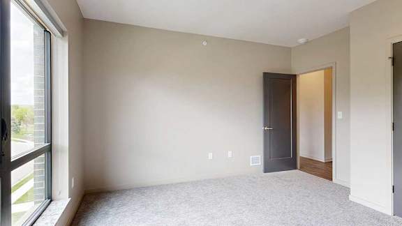 A bedroom with a large floor-to-ceiling window, and carpeted flooring.