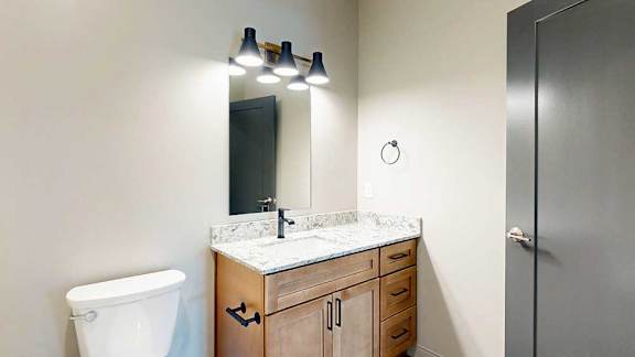 A bathroom with a warm wooden cabinets, white quartz vanity sink, and a mirror with overhead lighting.